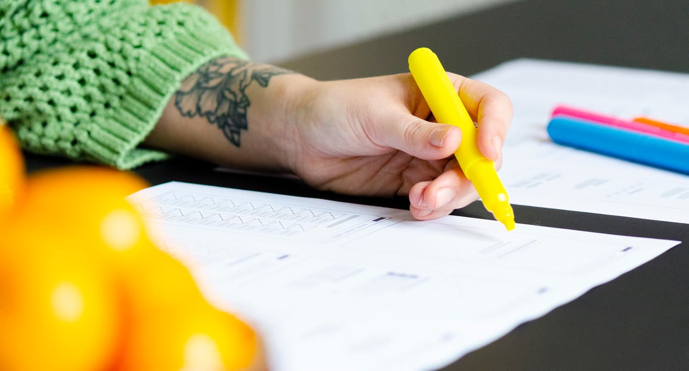 Bildet viser en hånd som holder en gul tusj som tegner på et ark med wireframes. Det er flere fargerike tusjer og ark på bordet.