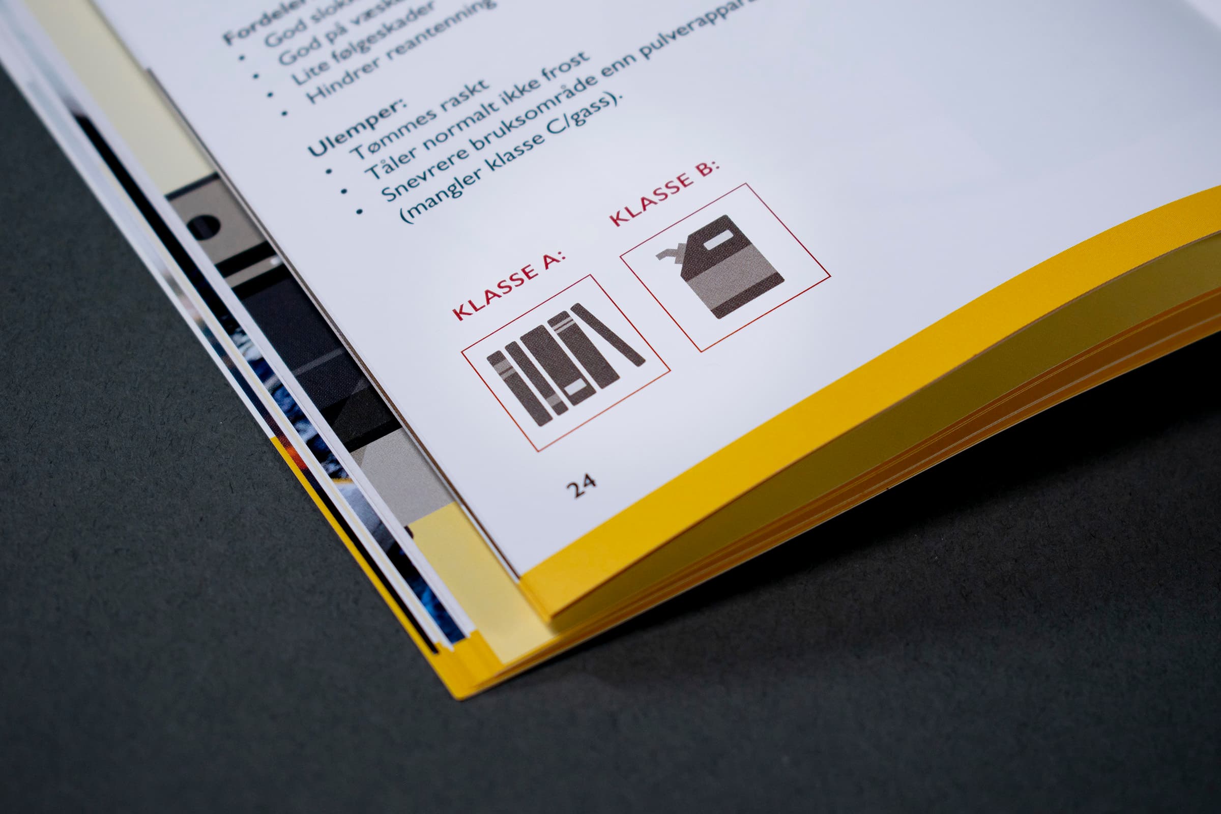 Bildet viser et nærbilde av en side i en bok. Den er en gul stripe nederst på siden. Det er tekst på siden, og nederst er det to ikoner som indikerer "klasse A" og "klasse B"