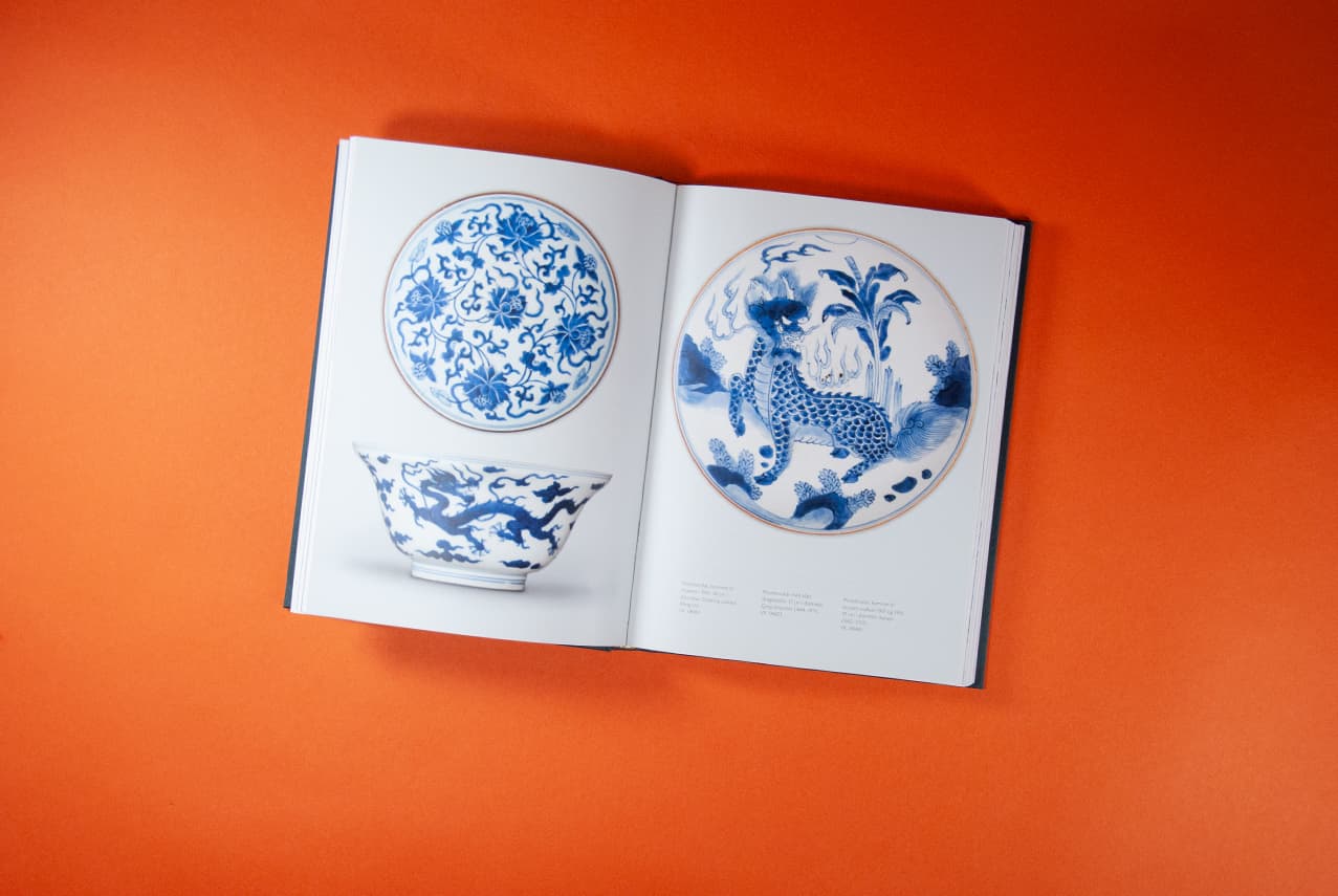 Bildet viser et oppslag av boka tatt ovenfra. På begge sider er det bilder av ting med blått mønster. På venstre side en tallerken og en skål, mens det på høyre side er bilde av en større tallerken som fyller siden i bredden.