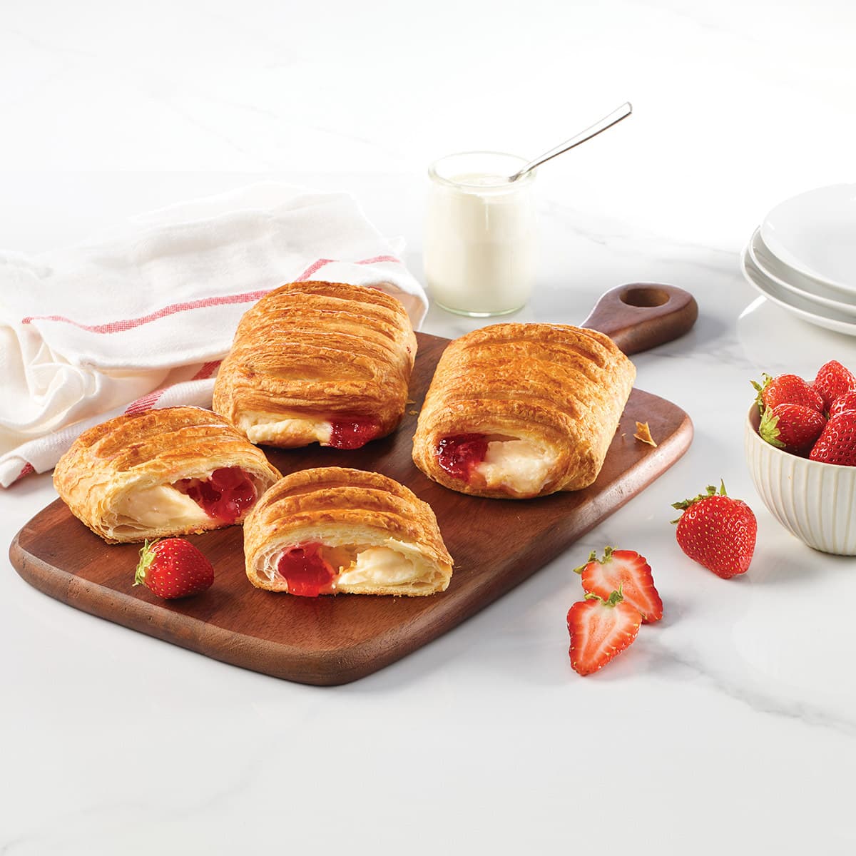 four cream cheese and strawberry danishes on a board