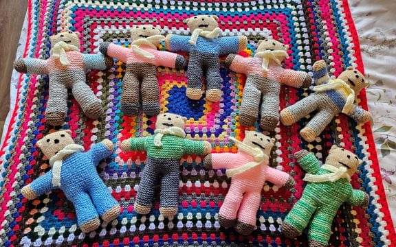 Knitted bears in different colours laying next to each other on a blanket at care home in Sudbury