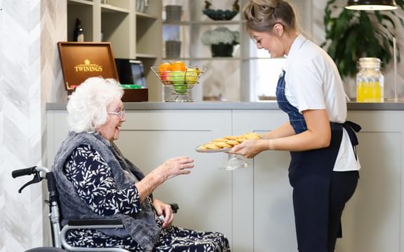 Elderly care home resident in a wheelchair taking baked treats from a care home team member.