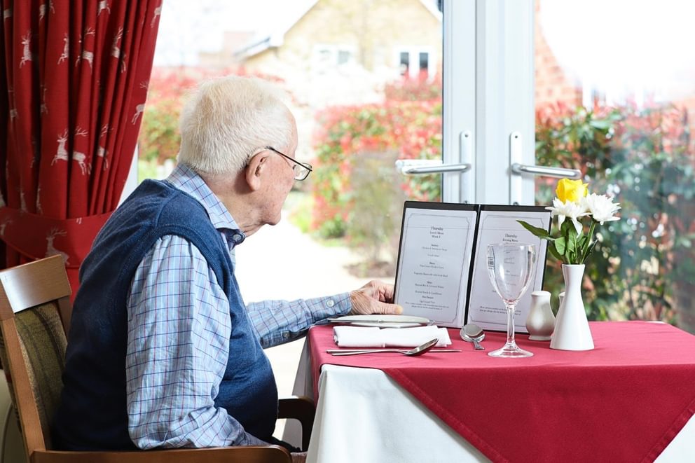 An elderly resident at Caring Homes care home reading a dinner menu seated at a table