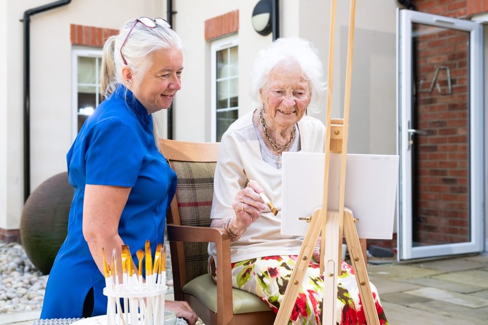 Resident painting in the garden with Activities lady smiling front angle
