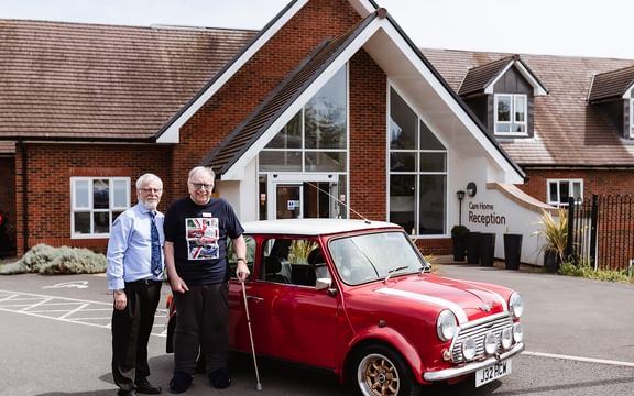 Resident and Home Manager standing next to red Mini Cooper