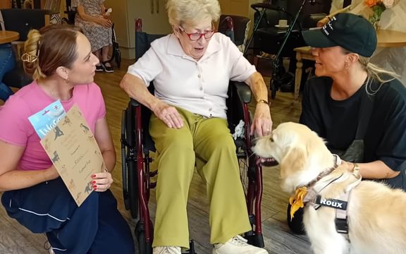 Care home resident in a wheelchair with two ladies and a dog