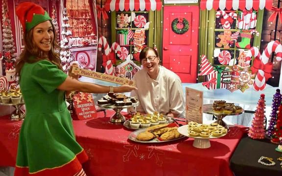 Care home team member in elf costume in front of a festive food stall