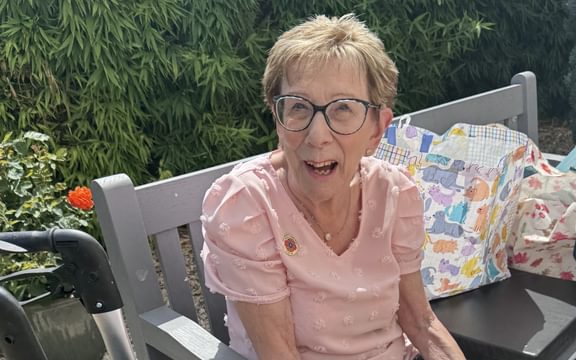 Smiley female care home resident sitting on a bench in the sun