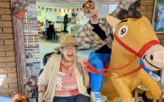 Care home resident dressed in cowboy hat next to carer on an inflatable horse