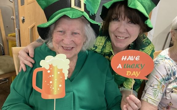 Resident and carer wearing green tops and hats, holding St Patrick's Day themed signs