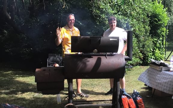 Two men cooking at a double barbecue in a care home garden