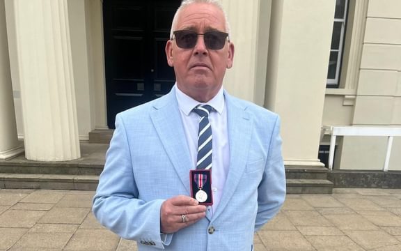 Male in blue jacket and tie holding medal in box