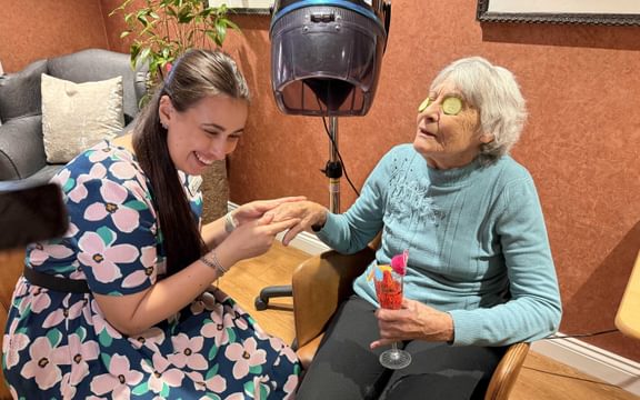 Care home resident having a hand massages and a mocktail in a care home beauty salon