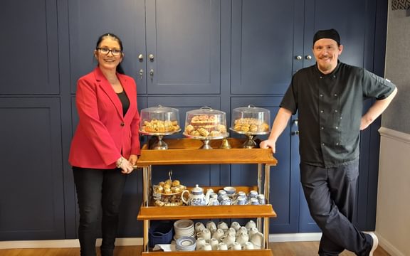 Care home manager and chef with a high tea trolley piled high with cakes