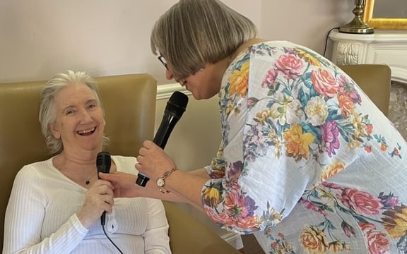 Care home resident smiling and holding a microphone with singer
