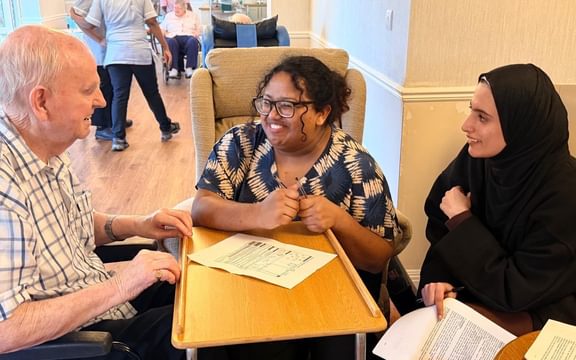 Care home resident talking to 2 smiling students at a desk