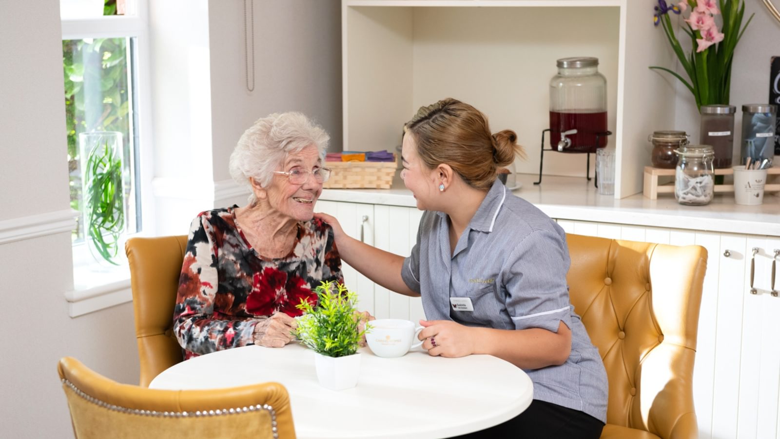 Female resident having a cup of tea with a carer in a bistro setting within a care home
