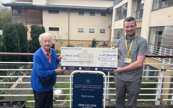 Female care home resident hands over cheque to Marie Curie representative