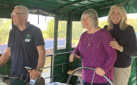 Female care home resident drives canal boat with two others in shot