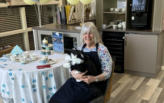 Care home resident at forget-me-not decorated table with black and white robotic cat