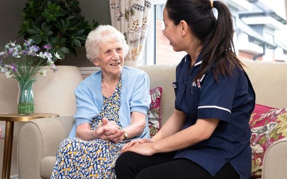 Nurse sitting with care resident smiling while receiving nursing care