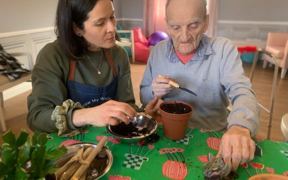 Care home resident preparing a plant pot with earth as part of an activity