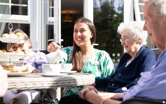 A group of happy care home residents and a care home team member enjoying an afternoon tea in a garden.