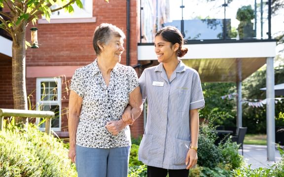 Resident and carer walking through a care home garden for Caring Homes Group Parkinson's event