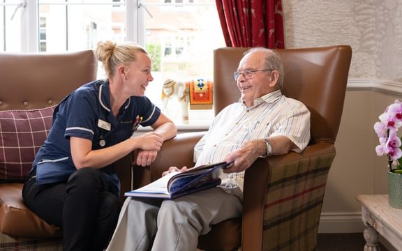 Caring homes resident sat in a brown leather armchair talking to one of their nurses.
