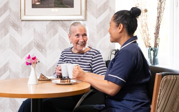 A Registered Nurse at a Caring Homes nursing home having tea and cake with a resident.