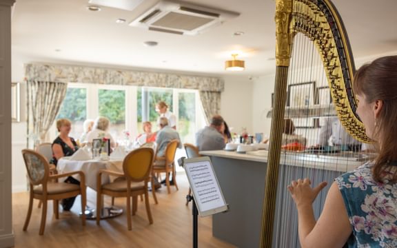 Musician playing a harp in front of residents enjoying refreshments.