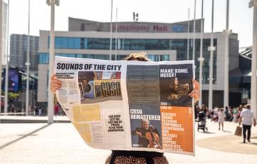 Photograph of somebody reading the CBSO Newspaper outside Symphony Hall