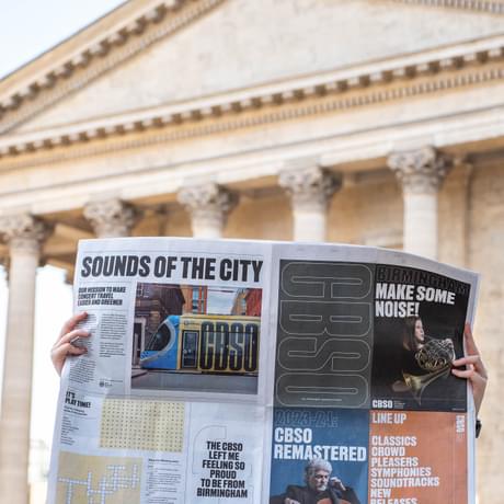 Photograph of somebody reading a CBSO newspaper in front of Birmingham Town Hall.