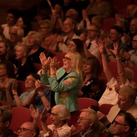A photograph of a woman giving a standing ovation in Symphony Hall