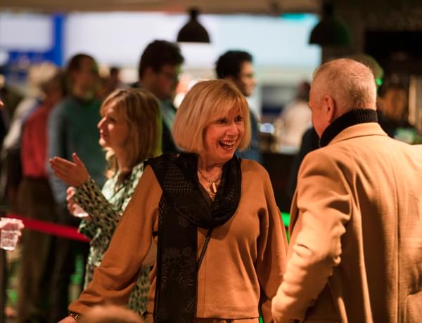 Photograph of a woman smiling and talking to a friend in the Symphony Hall foyer