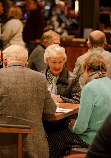 Photograph of a group of friends sitting and talking at a table in the Symphony Hall foyer