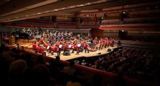 Photograph of the orchestra performing at Symphony Hall wearing brightly coloured polo shirts