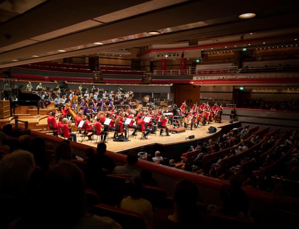 Photograph of the orchestra performing at Symphony Hall wearing brightly coloured polo shirts