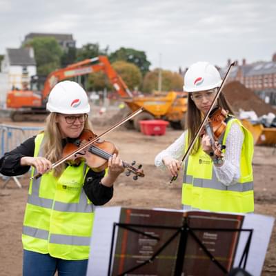 Photograph of Charlotte Skinner and Bryony Morrison playing the violin at the building site of the Shireland CBSO Academy