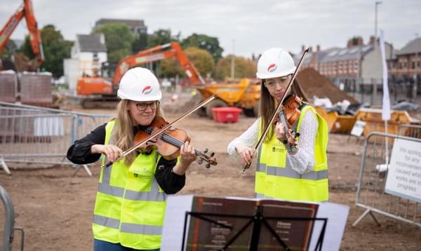 Photograph of Charlotte Skinner and Bryony Morrison playing the violin at the building site of the Shireland CBSO Academy