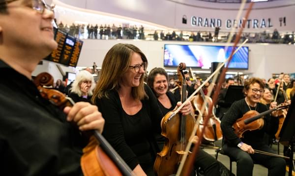 Photograph of Amy Thomas and the viola section laughing whilst performing in New Street train station
