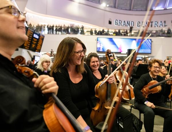 Photograph of Amy Thomas and the viola section laughing whilst performing in New Street train station