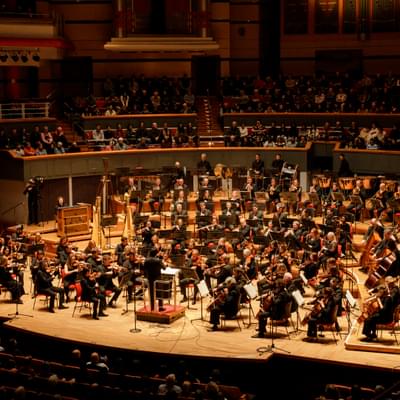 Photograph of the full orchestra performing to a packed audience at Symphony Hall