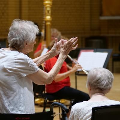 Photograph of an elderly woman giving a standing ovation to a small ensemble of players