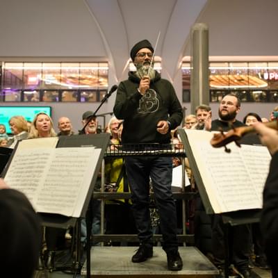 Photograph of a member of the public conducting the orchestra at New Street Station