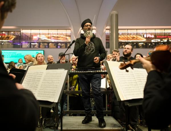 Photograph of a member of the public conducting the orchestra at New Street Station