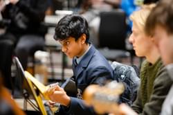 Photograph of a teenage boy in school uniform playing the guitar in a Project Remix rehearsal