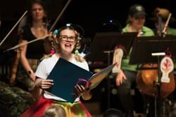 Photograph of Charlotte Skinner presenting a Key Stage 1 concert wearing a brightly coloured outfit