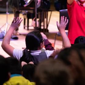 Photograph of a child holding their hands above their head as they watch a Relaxed Concert