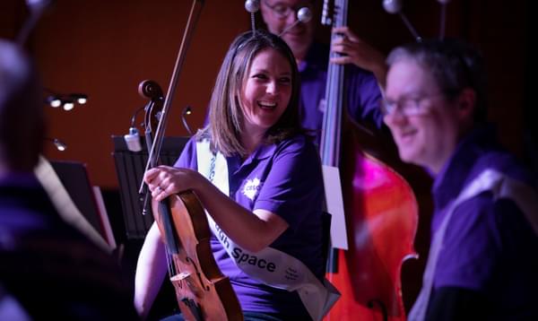 Photograph of Amy Thomas and other musicians wearing headbands with baubles on and laughing as part of a Key Stage 1 concert